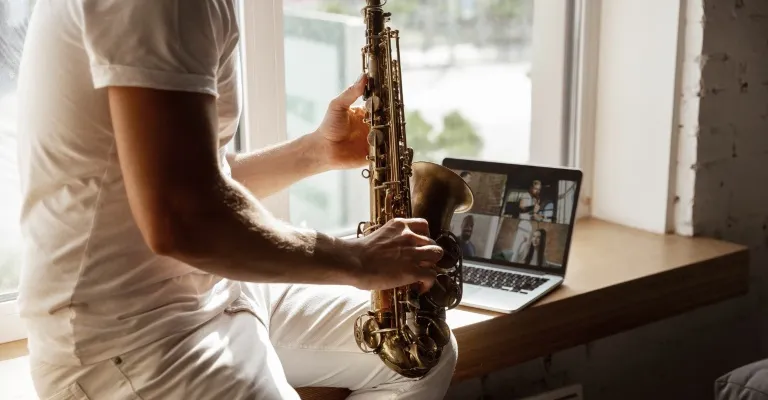 man playing saxophone in front of a laptop